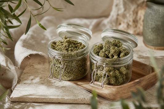 CBD Blüten mit unterschiedlich trockenem und feuchtem Eindruck in zwei neutralen Glasbehältern